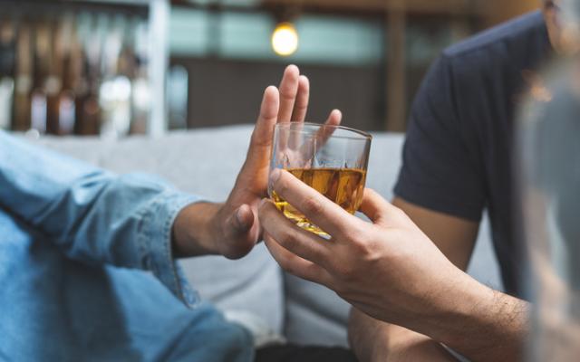 Persona con intolerancia al alcohol rechazando con la mano un vaso de licor